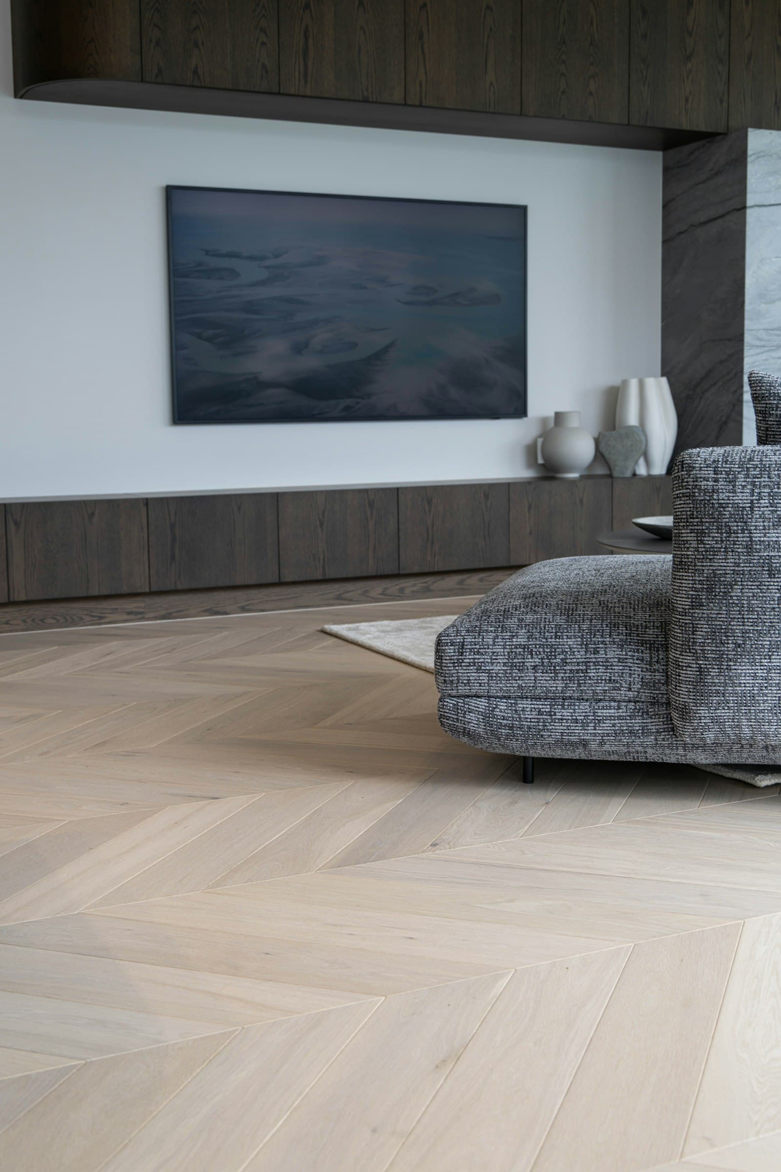 Wohnraum mit Fischgrätparkett, Sofa und Kunstwerk an der Wand